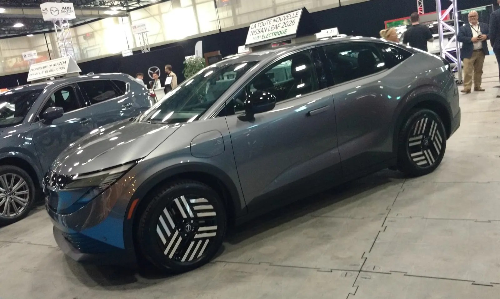 Gray 2026 Nissan Leaf viewed from the front quarter at an auto show in Quebec