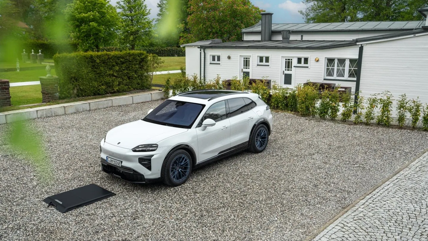 White Cayenne Turbo Electric beside a black wireless charging floor plate on a parking area.
